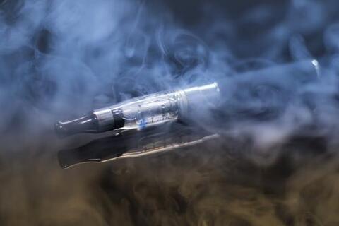 Stock photo of an e-cigarette device lying on a surface surrounded by smoke and vapour.