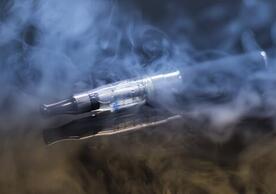 Stock photo of an e-cigarette device lying on a surface surrounded by smoke and vapour.